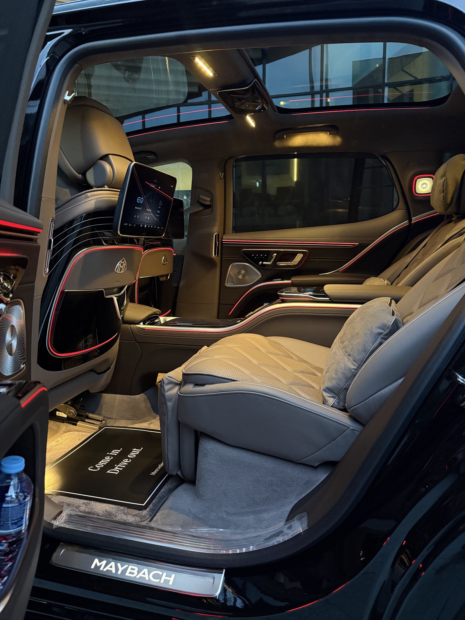 Maybach EQS rear cabin through the open left door — one reclined quilted seat and its seatback screen