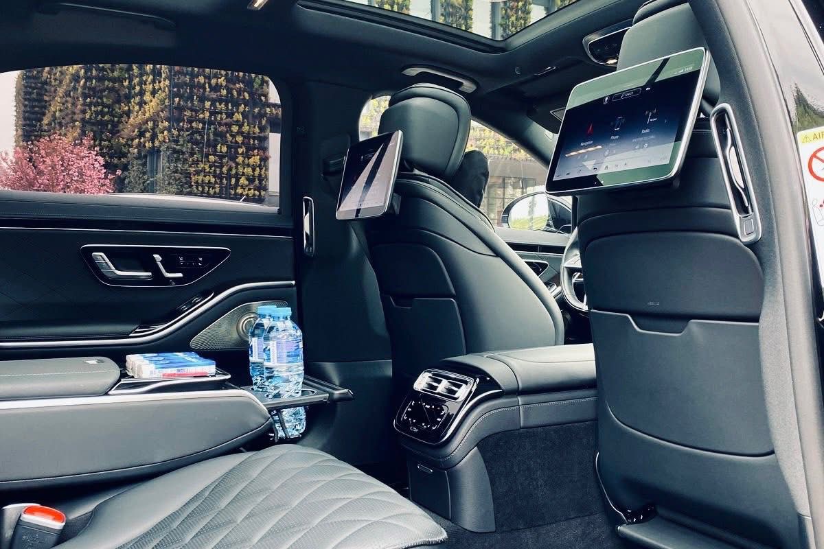 Interior of a Mercedes S-Class rear cabin: cream leather, the rear-seat screen, sunroof and ambient lighting.