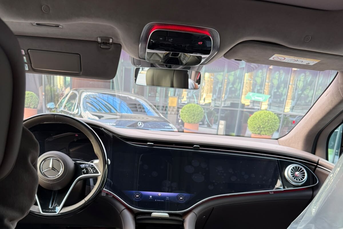 The front cabin of a Mercedes-Maybach EQS: the steering wheel, the full-width dashboard screen and a city street through the windscreen.