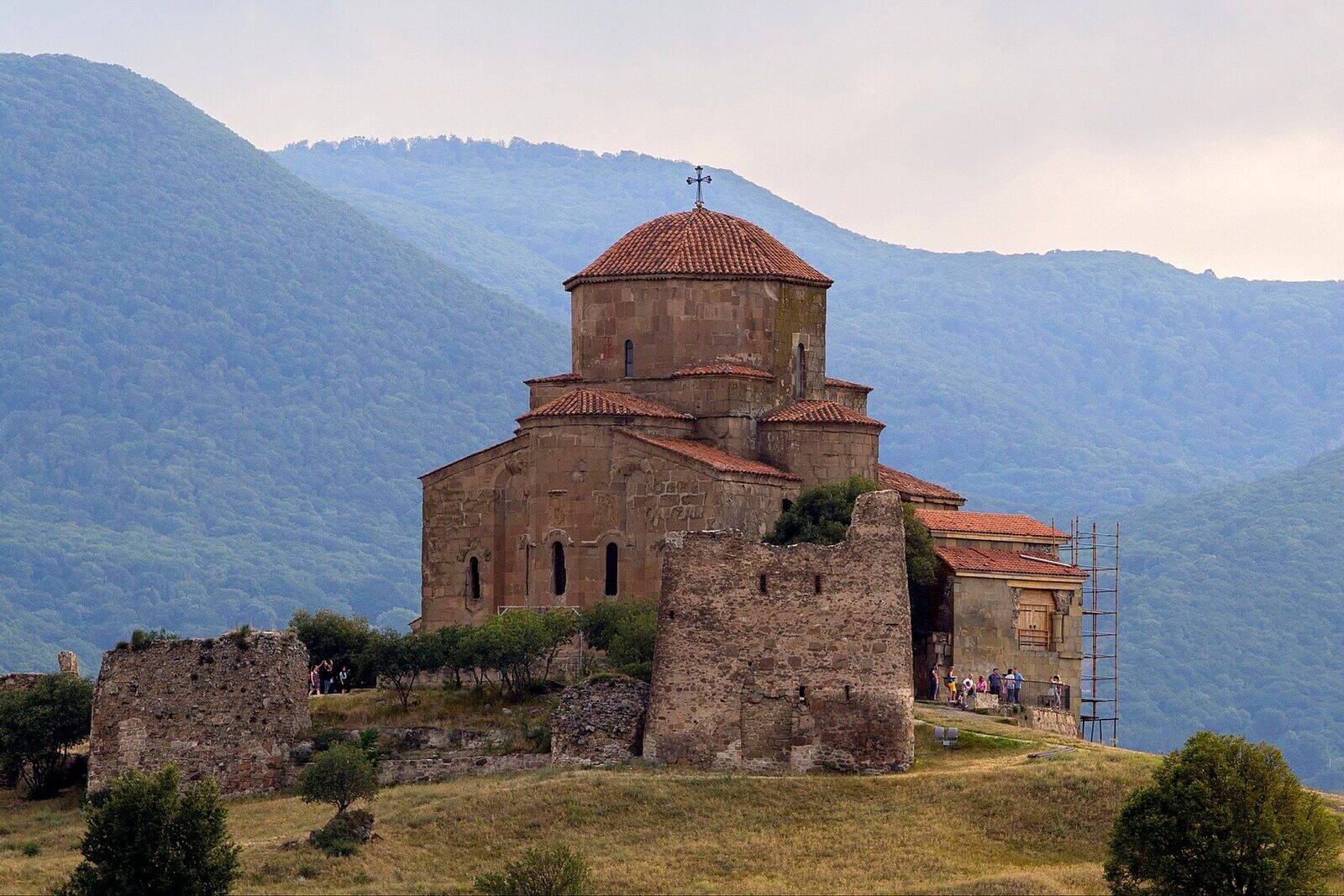 Jvari Monastery's domed stone church on its hilltop above Mtskheta, with wooded mountains behind it.