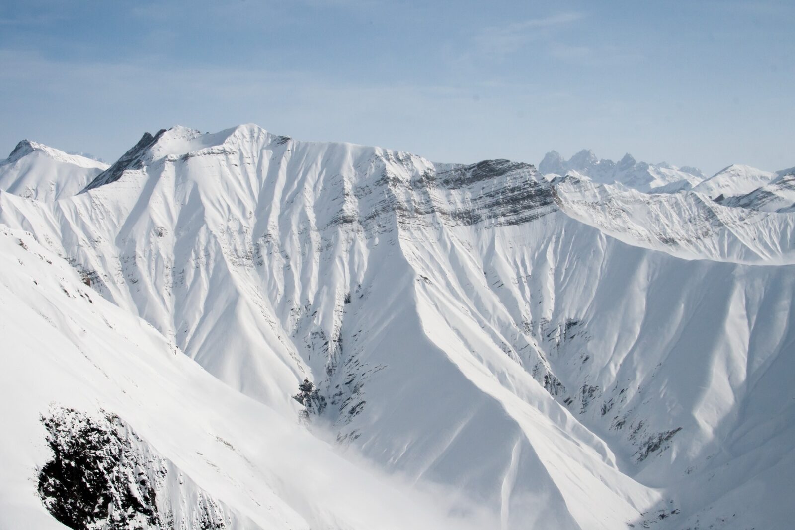 Snow-covered Caucasus ridges above Gudauri under a pale winter sky, bare rock showing through on the steepest faces.