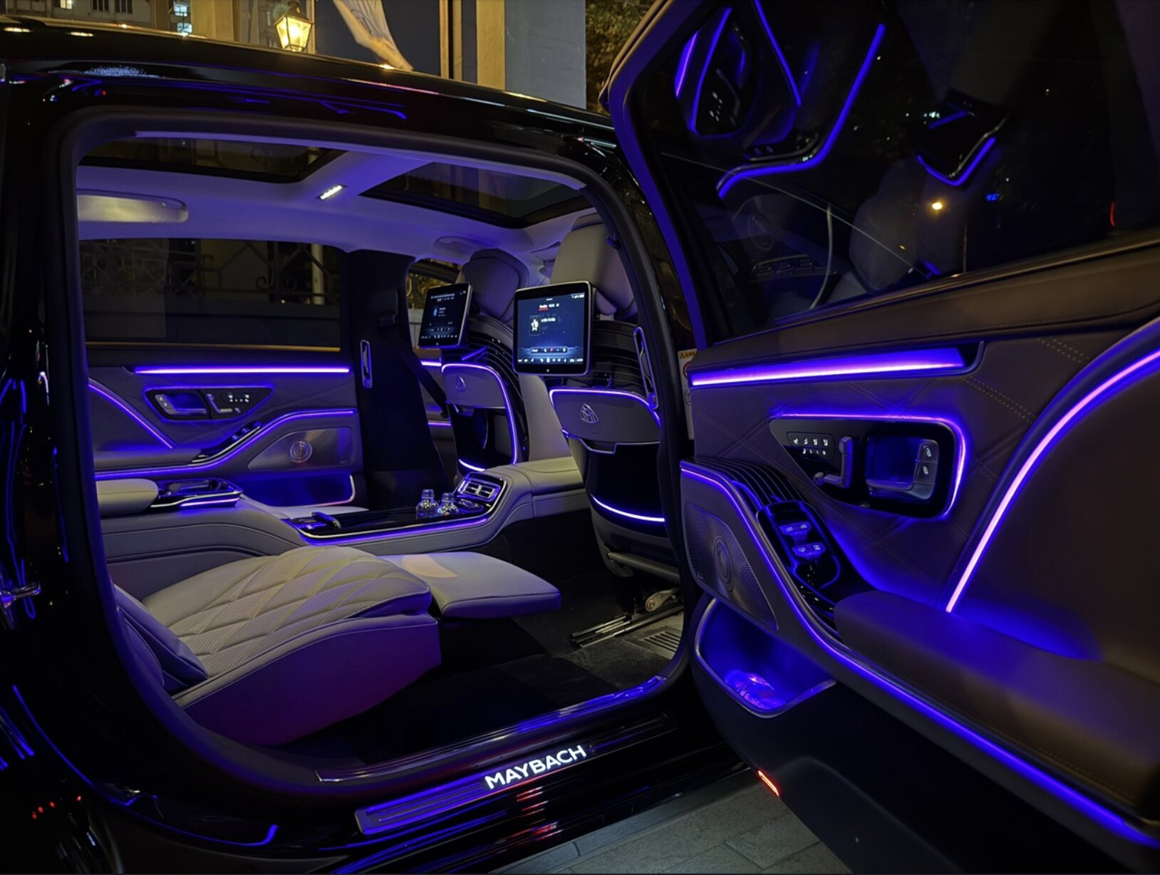 Maybach SOIT с открытой задней дверью при ночном прибытии, тёпло освещённый салон на фоне тёмного фасада тбилисского отеля.
