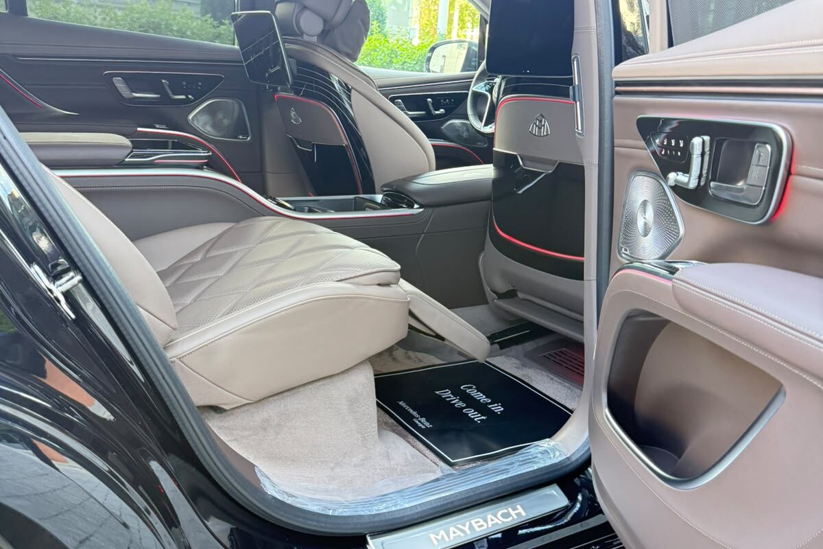 The rear door of a Mercedes-Maybach EQS 680 standing open on a light quilted seat, a floor mat and the MAYBACH sill plate.