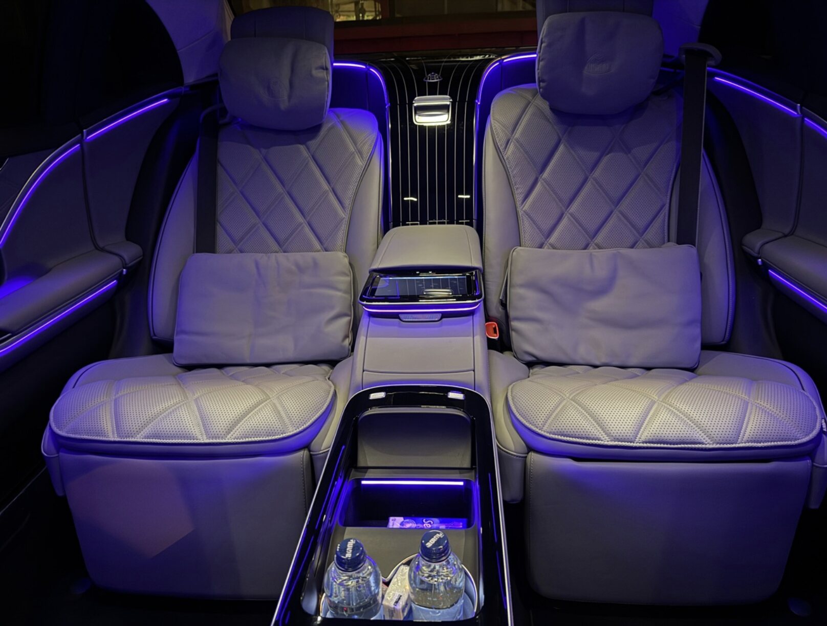 Mercedes-Maybach rear cabin in cream Nappa leather with diamond-stitched seats, central console, and purple ambient lighting.