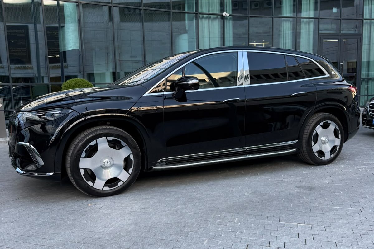 A black Mercedes-Maybach EQS 680 in side profile, parked outside a glass-fronted building in Tbilisi.