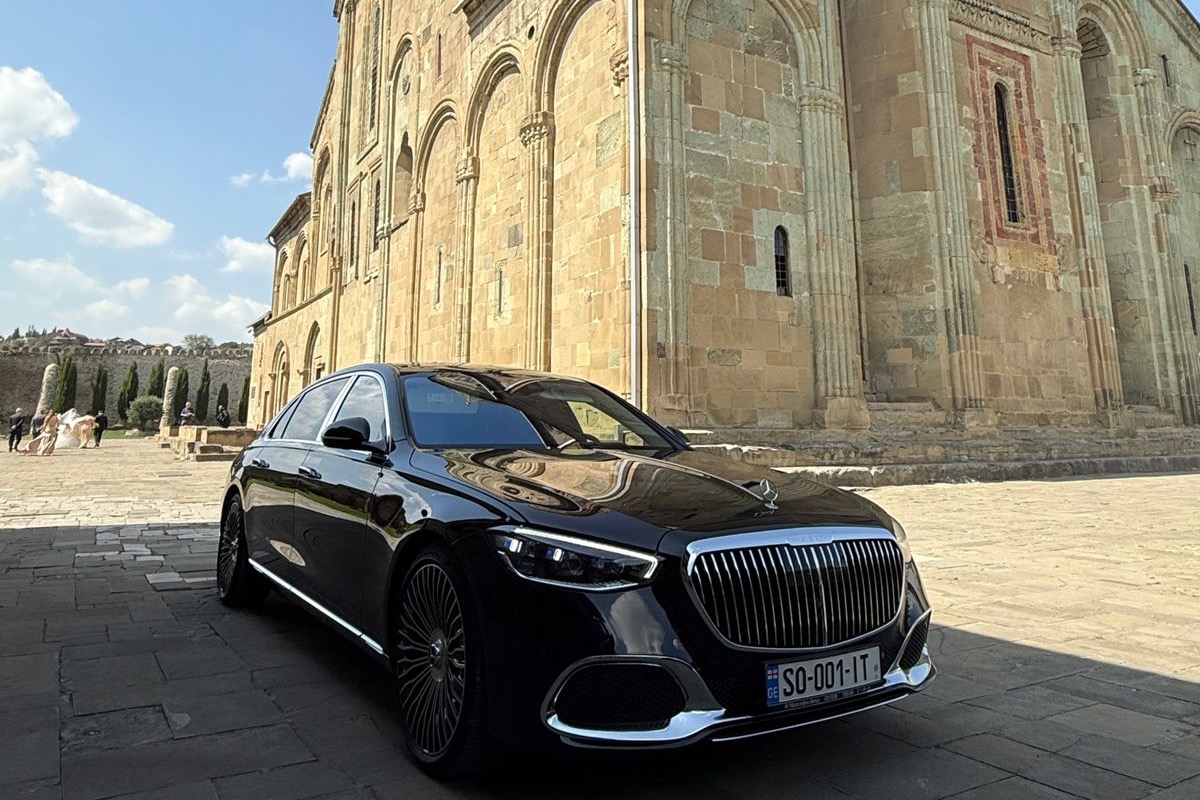 A black Mercedes-Maybach parked beside Svetitskhoveli Cathedral in Mtskheta, the cathedral's stone facade rising behind it.