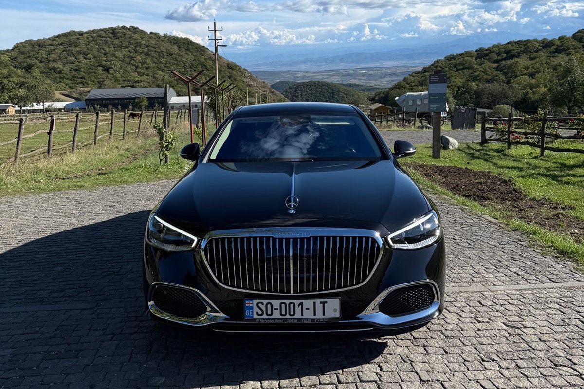 A black Mercedes-Maybach S-Class at a cellar entrance in the Kakheti hills, the Alazani valley unfolding beyond the fence.