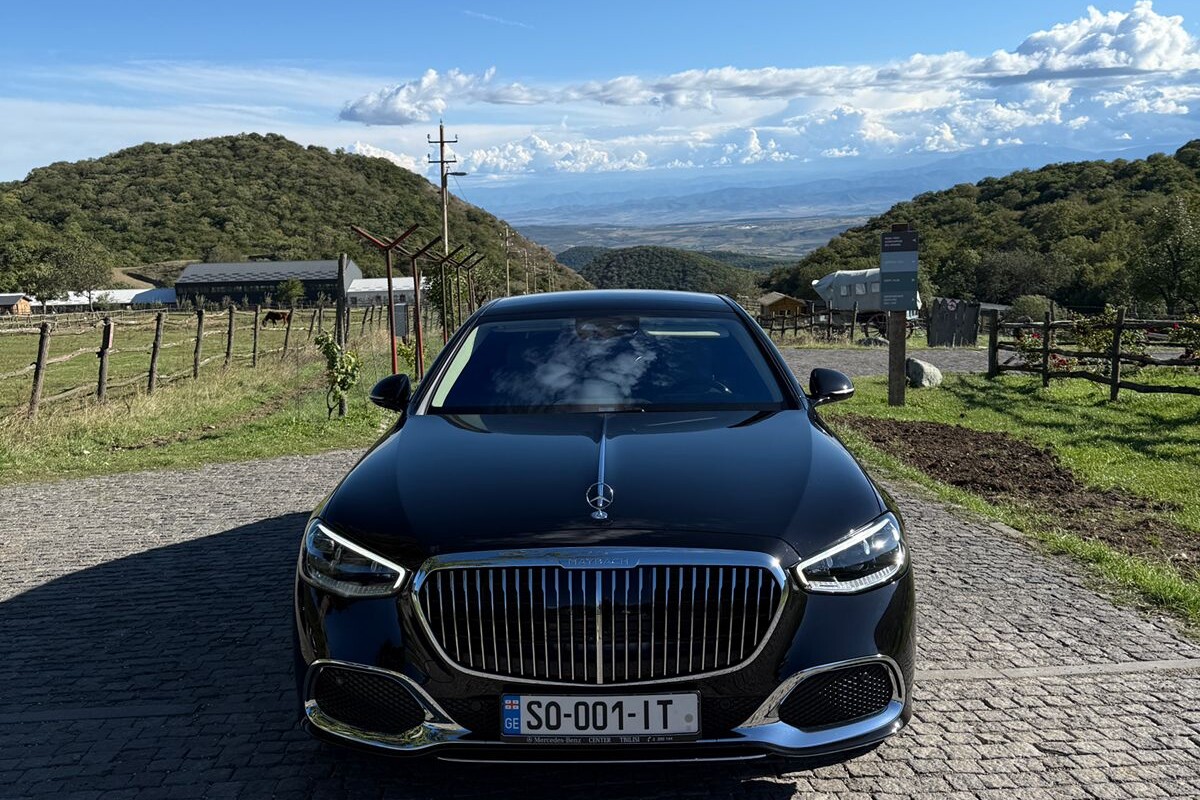 A black Mercedes-Maybach on a stone-paved driveway overlooking a Kakheti vineyard and the Alazani valley beyond.