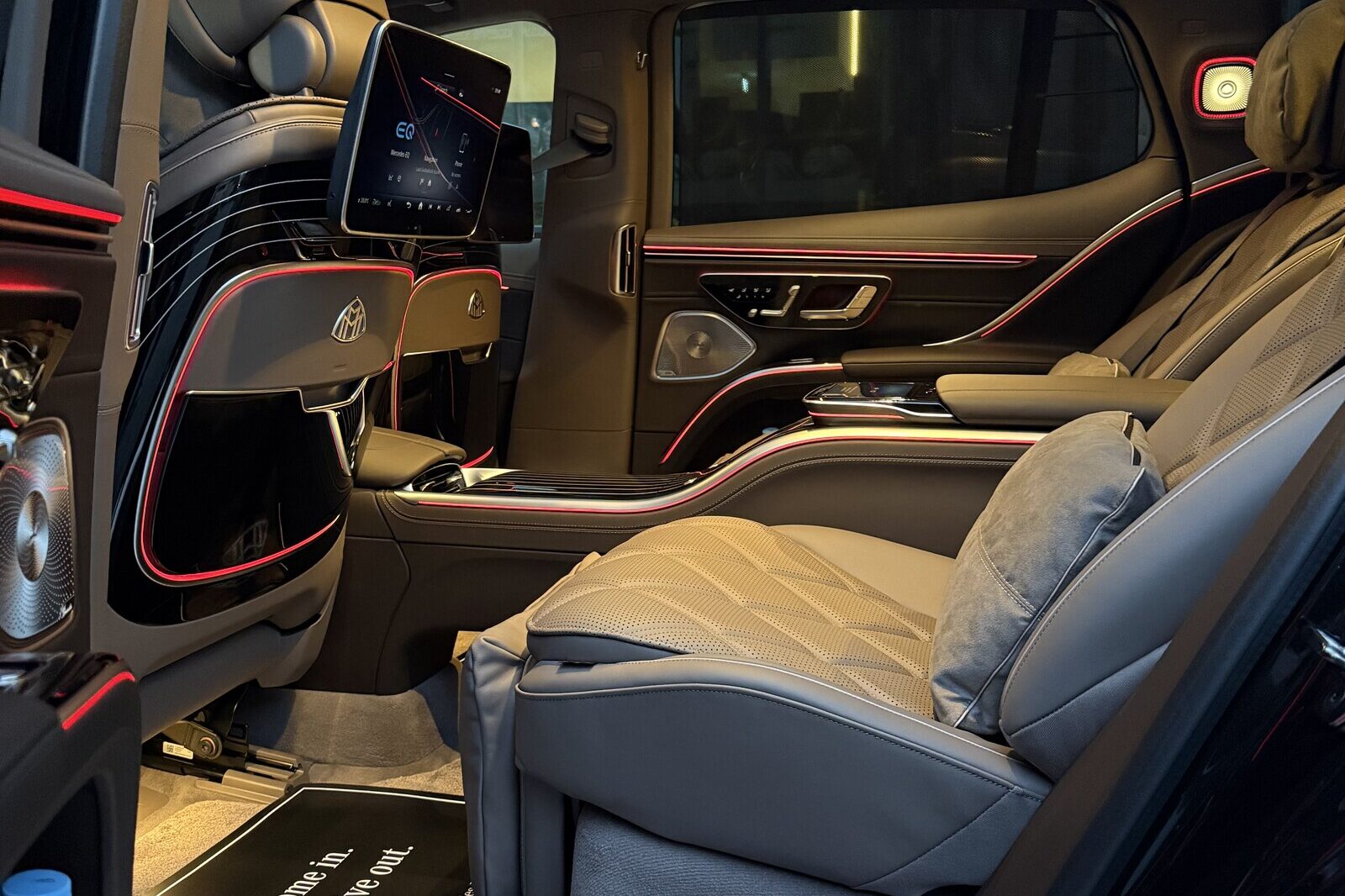 The rear cabin of a Mercedes-Maybach EQS through the open left door: a reclined quilted seat with a cushion, and a seatback screen ahead.