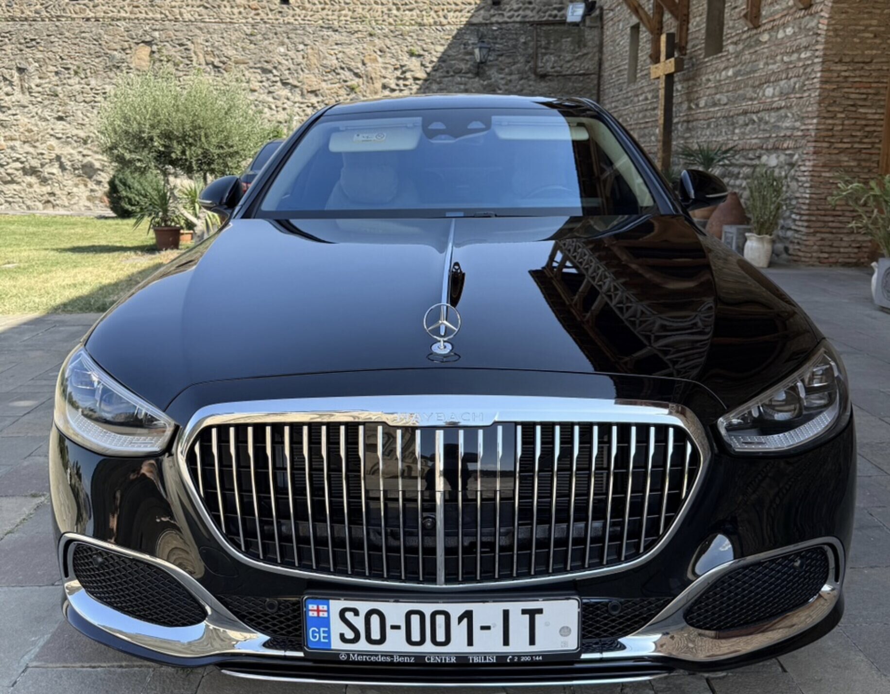 A black Mercedes-Maybach seen head-on, parked on stone paving beside an old fortress wall in daylight.