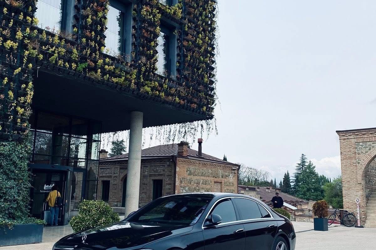A SOIT S-Class parked outside Stamba Hotel in Tbilisi, the historic stone facade and contemporary glass entrance behind.
