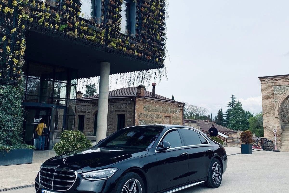 A black Mercedes-Benz S-Class at the entrance of Stamba Hotel in Tbilisi, the building's vertical garden facade rising behind it.