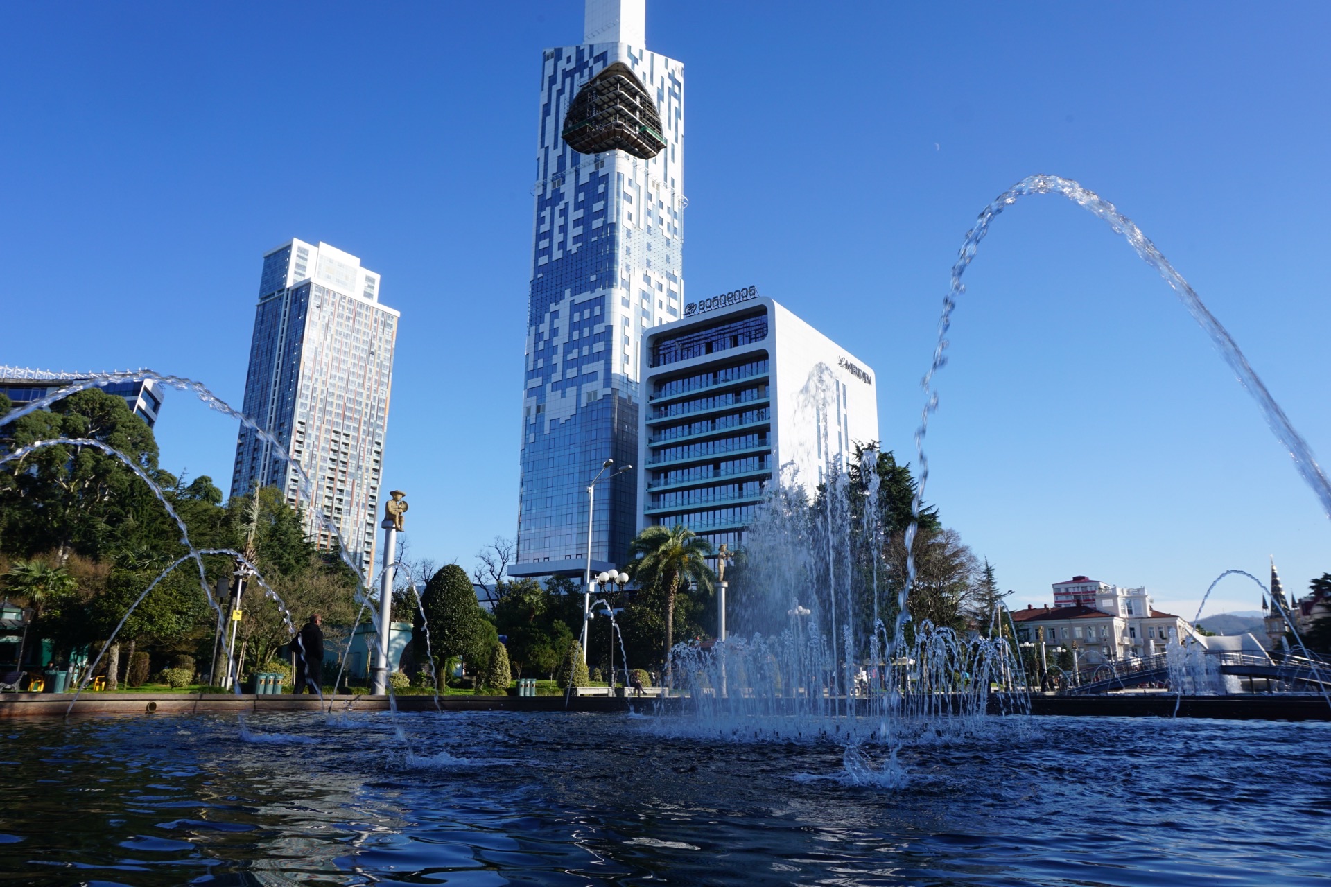 The seafront boulevard at Batumi, palm trees along the promenade with the Black Sea beyond and apartment towers behind.