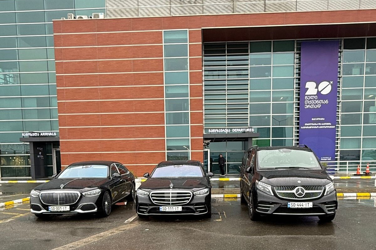 Three black Mercedes vehicles — a Maybach, an S-Class, and a V-Class — parked together in front of Tbilisi International Airport's arrivals and departures.