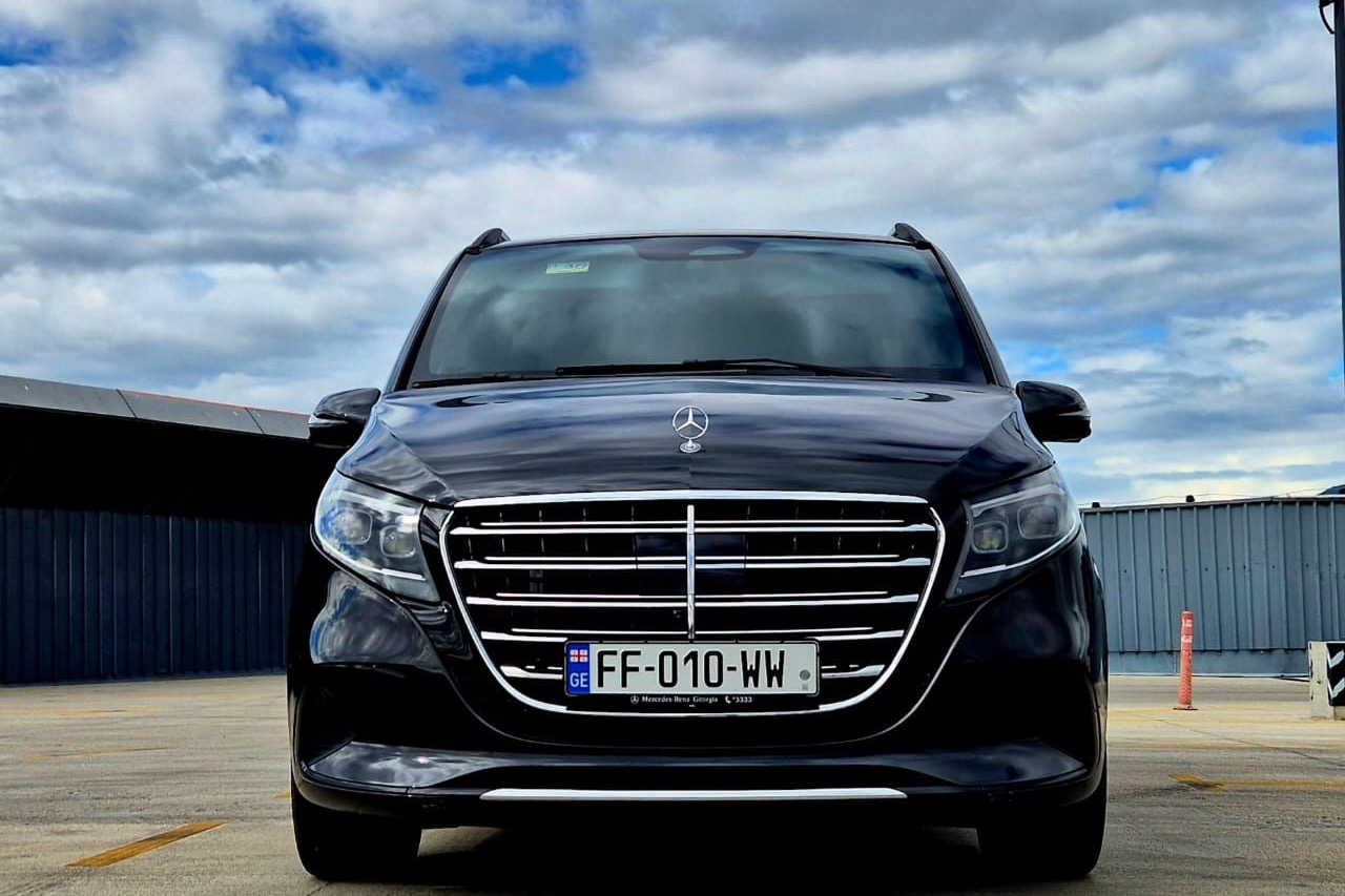 Чёрный Mercedes-Benz V-Class анфас на тбилисском аэродроме, яркая облачность над ним.